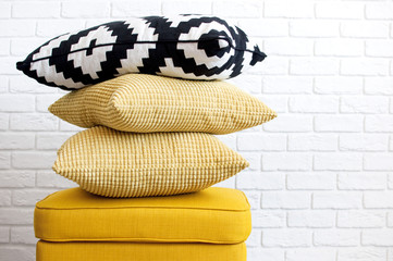 Yellow puff with pillows against a white brick wall. Concept Interior Things Copy Space.