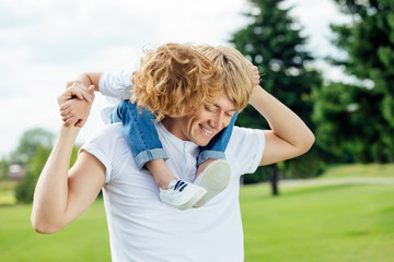 Naklejka premium happy young father carrying adorable little son on neck while walking in park