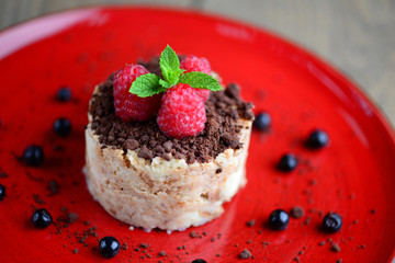 A delicious dessert with fresh raspberries and chocolate chips on a red plate. Blurred background.