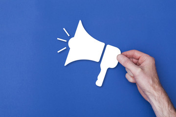 male hand holding a loud speaker icon symbol against a blue background