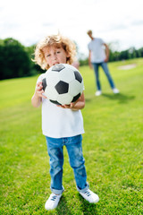 adorable little boy holding soccer ball and looking at camera while playing in park