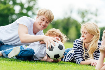 happy family with two kids having fun with soccer ball while lying on green meadow