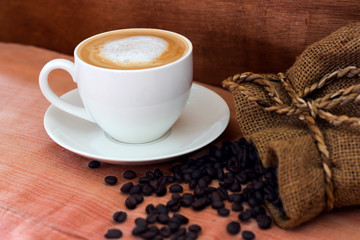 Coffee in a white cup and coffee beans on the table.