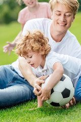 happy father and son playing with soccer ball on green grass at park