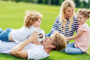 Fototapeta na wymiar happy family with two kids having fun with soccer ball while lying on green meadow