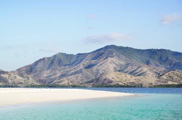 Foto op Canvas Empty white sand beach with blue ocean during the day overlooking mountain landscape with green vegetation in te ocean, Flores Indonesia. © Eduard