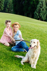 Obraz premium beautiful happy mother and daughter with golden retriever dog resting on green meadow in park
