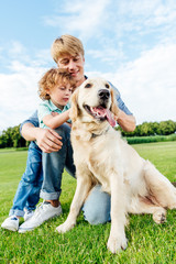 happy father and son stroking golden retriever dog at park