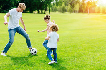 young father with cute little children playing soccer on green grass in park