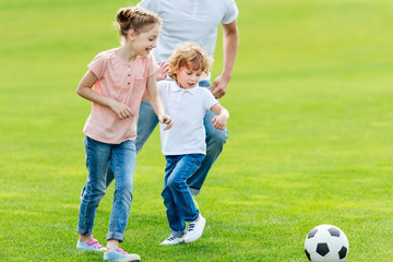 cropped shot of father with happy kids playing soccer in park