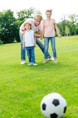 Fototapeta premium young father with adorable little kids looking at soccer ball on green lawn