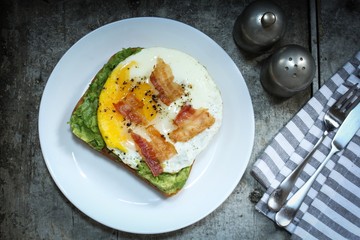 Avocado bread egg toast  topped with bacon and pepper, top down view