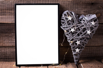 One empty  black frame and decorative heart with fairy light  on  wooden background.