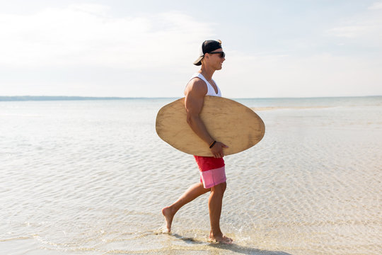 happy young man with skimboard on summer beach