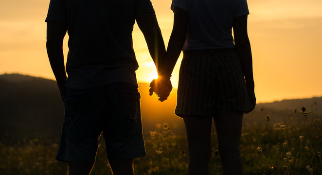 Couple holding hands and watching the sunset, silhouette