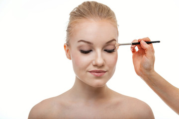 Fototapeta premium Makeup artist applying eye shadow for beautiful young woman on white background