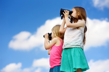 Two cute little girls looking through binoculars on sunny summer day