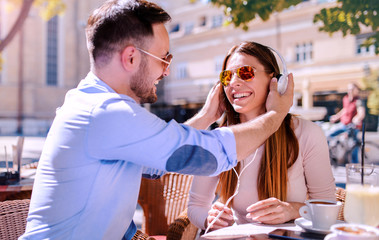 Dating in the cafe. Young couple drinking coffee and listening to music with headphones. Love, dating, technology, lifestyle