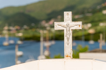 White cross in a cemetery in Martinique with sailboats and sea in background