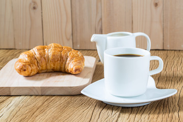 Coffee cup and croissant on wooden table