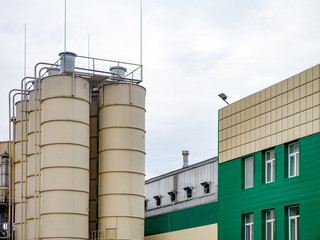  Industrial building external view with tanks, blue sky. Green and white front
