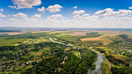 Fototapeta na wymiar Beautiful view of a typical Ukrainian village surrounded by fields, green forests, small river and blue sky with white clouds. Aerial view.