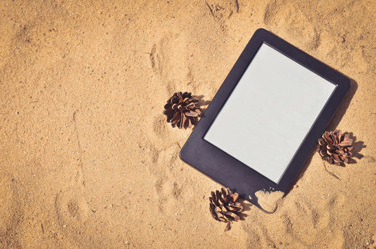E-book reader on the beach sand. Toned image. Copy space. Top view.