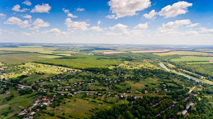 Beautiful view of a typical Ukrainian village surrounded by fields, green forests, small river and blue sky with white clouds. Aerial view.