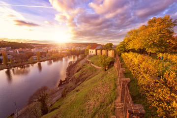 Autumn in Prague, golden sunset at Vyshehrad. Panoramic view to the fortress wall, Vltava river and city of Prague with blue cloudy sky and sun, travel Europe concept, Czech Republic