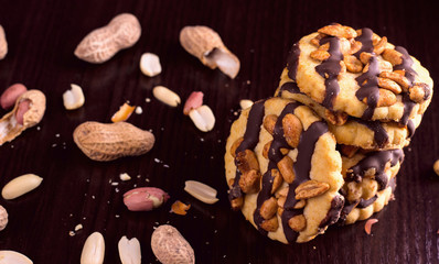 Cookies with peanuts, covered with chocolate icing, on a dark wooden background.