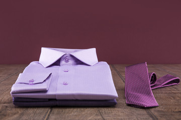 Lilac man's shirt and lilac ties on a wooden table. Background burgundy.
