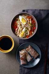Lunch with udon noodles cooked with vegetables and spring rolls. Top view. Composition with copy space on concrete background