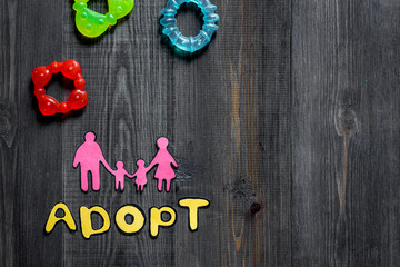 Adopt word, paper silhouette of family and toys on dark wooden table background top view copyspace