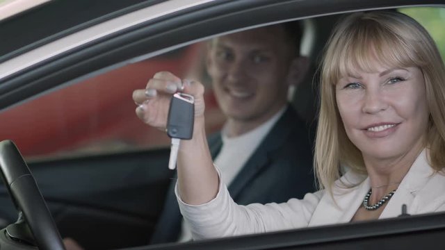 The salesman gives a car keys to happy businesswoman in car dealership