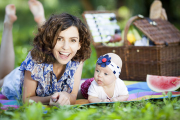 Young beautiful mother sits with her daughter on blanket in park.