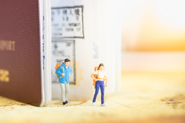 Two traveler miniature people figures with backpack standing and walking  out from passport with immigration stamps on world map. Travel and Journey concept.