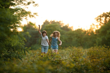 Little girl and boy are running in forest and holding hands.