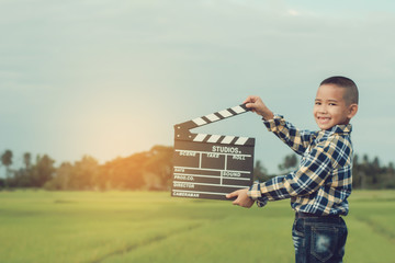 Kid playing film clapper board against summer sky background. Film director concept.