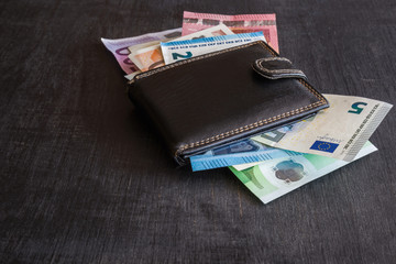Black, leather wallet with euro money on the dark wooden table. Money spending time.
