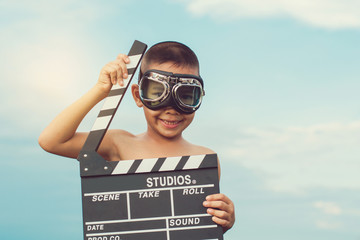 Kid playing film clapper board against summer sky background. Film director concept.