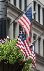 Three USA flags waving in the streets of Manhattan, two in a flower pot stand and one in a building