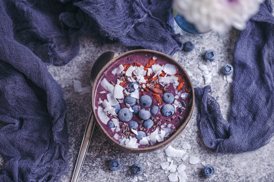 Blueberry smoothie topped with coconut flakes, goji berries, cacao nibs and blueberries in coconut bowl