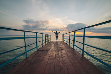 woman stands on the pier on sunrise with hands up