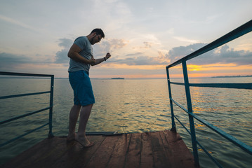 man rises hands up on the lake pier