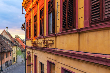 Fototapeta premium Detail of facade with shuttered old windows in ancient house on the street in Sibiu city, Romania, golden sunlight at sunset time