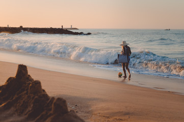 Naklejka premium Holiday lifestyle woman in straw hat on a beach holding bag. Recreational enjoyment walk along sunny outdoors background coastline. Idyllic remote relaxation seashore landscape