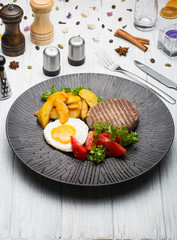 Fresh breakfast: fried potatoes with chop, ham and eggs on white wooden background.