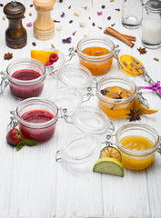 Jars with various jams and fruits on white wooden background.