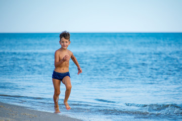 Fototapeta na wymiar Little boy running at the shore near sea