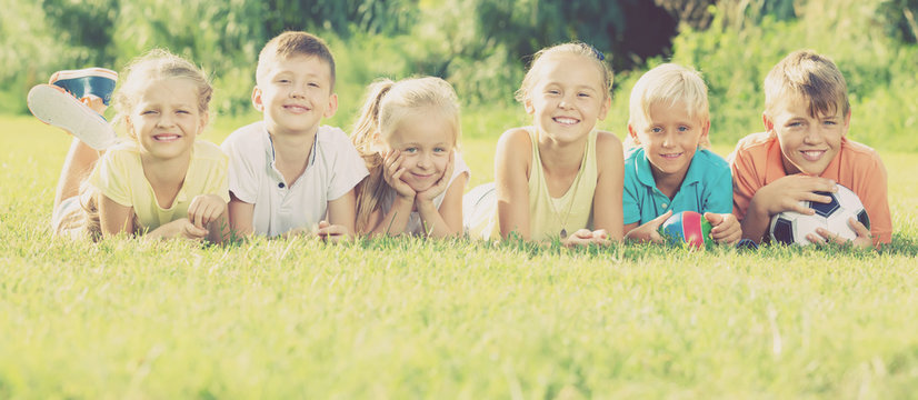 Group of friendly kids lying on green grass in park